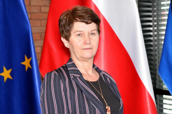Zdjęcie portretowe kobiety – krótkie ciemne włosy, ubrana jest w ciemną marynarkę z fioletowymi pionowymi paskami i czarną bluzkę.