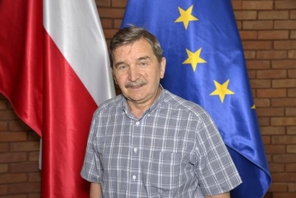 Zdjęcie portretowe mężczyzny – krótkie jasne włosy, wąsy, ubrany jest w szarą koszulę w białą kratę.