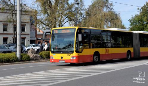 Ulica, po której jedzie czerwono-pomarańczowy autobus komunikacji miejskiej. Nad jego przednią szybą wyświetla się napis: 710.