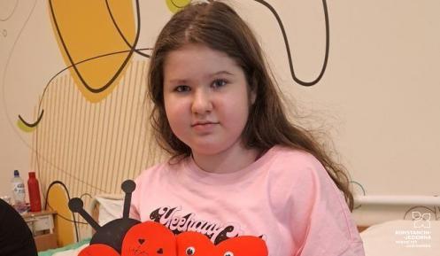 Dziewczynka z długimi, ciemnymi włosami, trzyma w dłoni wyciętą z papieru dużą biedronkę i serduszko.