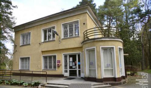 Jednopiętrowy budynek widziany z narożnika, po prawej strony obok wejścia półokrągła przybudówka , przed budynkiem schody