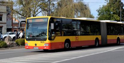 Ulica, po której jedzie czerwono-pomarańczowy autobus komunikacji miejskiej. Nad jego przednią szybą wyświetla się napis: 710 Piaseczno Targowisko.