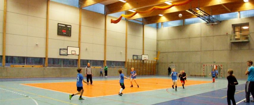 Zdjęcie hali sportowej, znajdującej się w Gminnym Ośrodku Sportu i Rekreacji. Na podłodze narysowane są różnego rodzaju linie, wyznaczające granice boisk do gry w kosza, piłkę nożną, siatkówkę itd. Na sali odbywa się trening dzieci w piłkę nożną.  