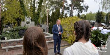 Dwoje uczniów tyłem, stojący przed pomnikiem, przed nimi przemawiający drugi zastępca burmistrza. 