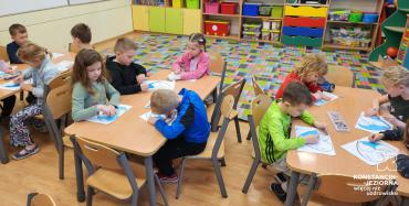 Dzieci siedzą w szkolnych ławkach i rysują ekologiczne plakaty. 
