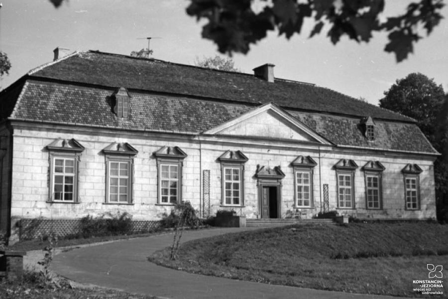 Czarnobiała fotografia dworu w Oborach (prostokątna bryła, zbudowany z cegłówek, nieotynkowany, na froncie 8 dużych okien z szotersami, do głównego wejścia prowadzą szerokie schody, dach spadzisty)