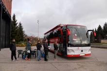 Na chodniku stoi czerwony autokar, z boku jest duży napis Mobilny punkt poboru krwi, obok jest godło Polski i napis Minister Zdrowia. Przed autokarem w kolejce stoi pięć osób.